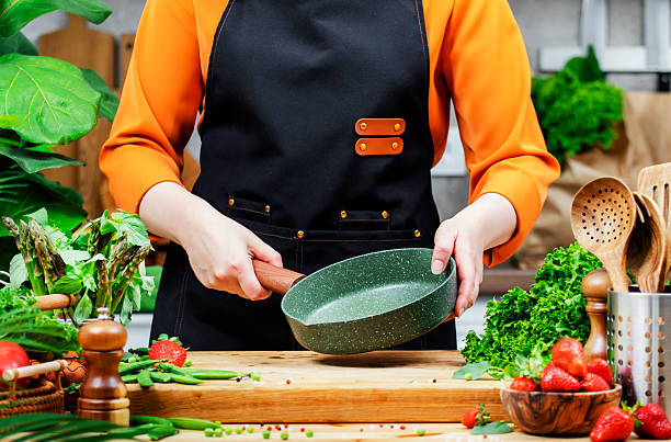 istock passionate female chef skillfully holds a green frying pan while surrounded by fresh vegetables and cooking utensils in a stylish kitchen. 2222536134