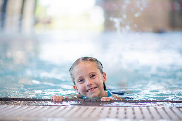 Young girl enjoying a swimming session in a vibrant indoor pool under soft natural light.