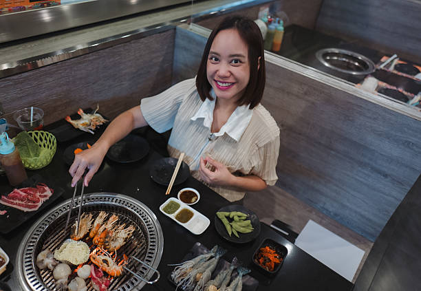Young woman grilling fresh seafood and tender meat while savoring authentic Japanese yakiniku barbecue in a cozy restaurant setting