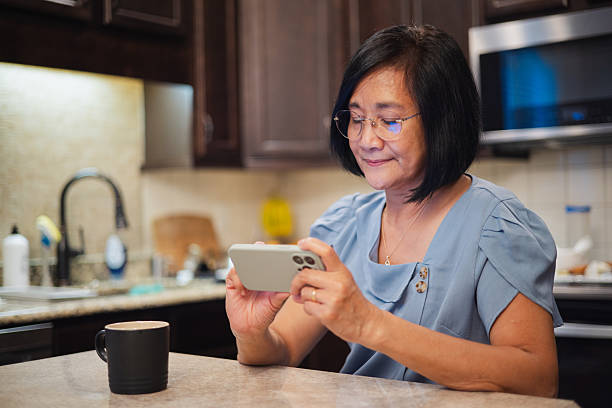 istock Using Phone in the Kitchen - Asian Woman - Sitting Looking At Phone - Focused 2222544426