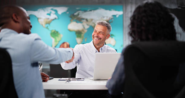 Happy Couple Smiling While Visiting Travel Agency Office To Choose Vacation Package. A Diverse Group Of People Handshake