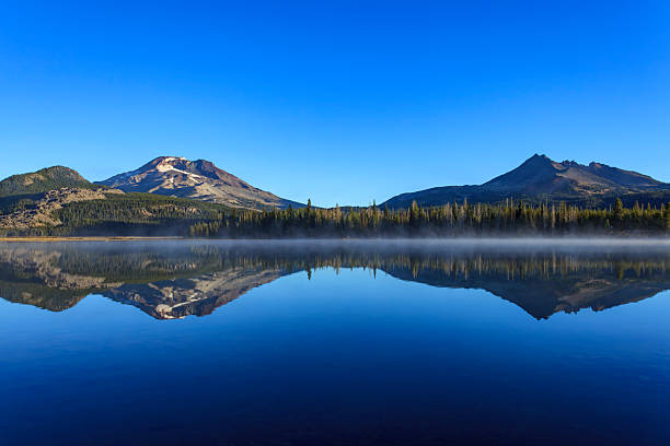 From Sparks Lake in Oregon (OR), South Sister and Broken Top rise above the water, reflecting in the calm alpine scenery.