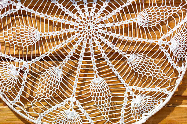 A white lace doily with a pattern of leaves and flowers. The doily is hanging on a wooden surface