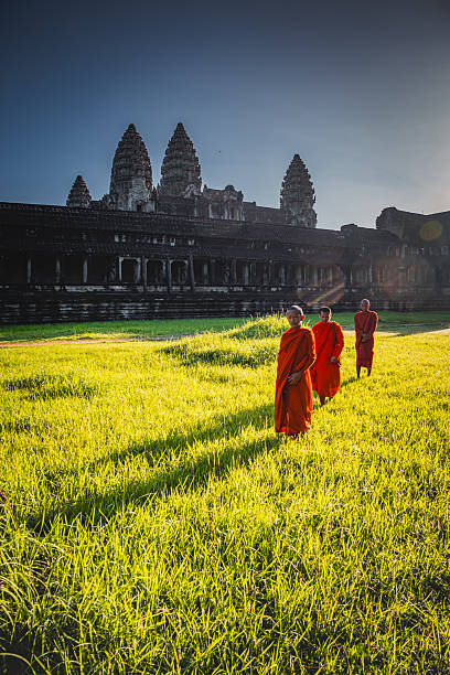 A local monk walks through the ancient stone structures of Angkor Wat, surrounded by lush greenery. The serene atmosphere highlights the temple's rich history and cultural significance in Cambodia.