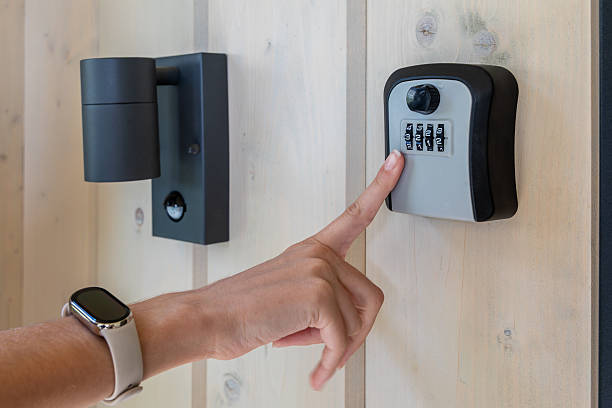 istock Hand entering code on outdoor key lock box. Close-up of a person inputting a combination code into a secure wall-mounted key lock box near a modern door and light fixture. 2222568105