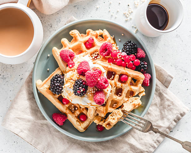 Overhead view of a plate of homemade waffles served with thick yoghurt, berries, quinoa puffs and syrup