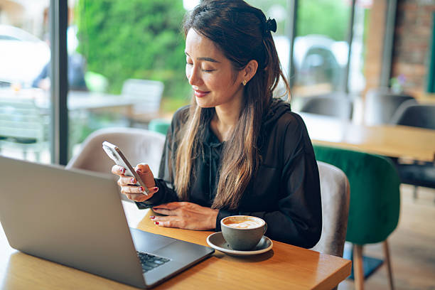 istock Asian woman using phone while working at coffee shop with laptop. 2222588509