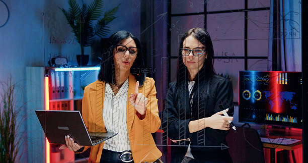 istock Accelerated shooting of attractive industrious experienced dark haired two female office workers which working together in the evening office and writing notes on transparent wall 2222594550