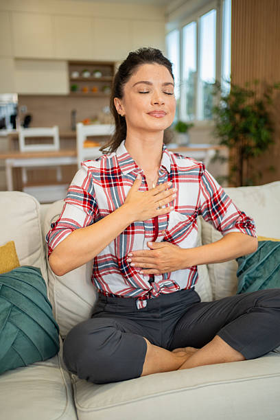 istock Serene woman practicing deep breathing exercise on sofa at home 2222598697