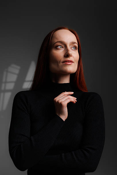 Long haired woman in black turtleneck on grey background with abstracted shadow