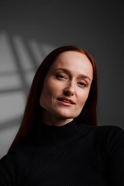 istock Smiling redhead woman looking at camera on grey background with abstracted shadow 2222603517