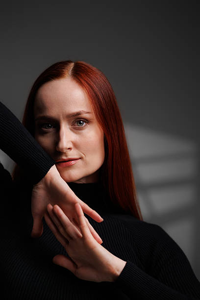 istock Redhead woman in black turtleneck looking at camera on grey background with abstracted shadow 2222603532