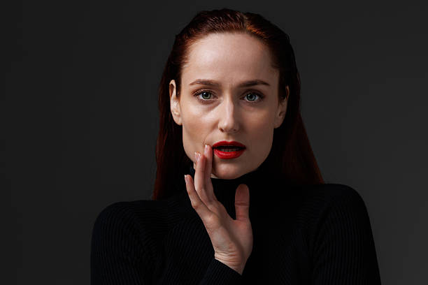 Redhead woman touching red lips isolated on grey