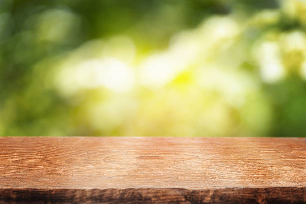 A smooth wooden tabletop set against a bright, sun-dappled green background, perfect for showcasing natural products or summer-themed content