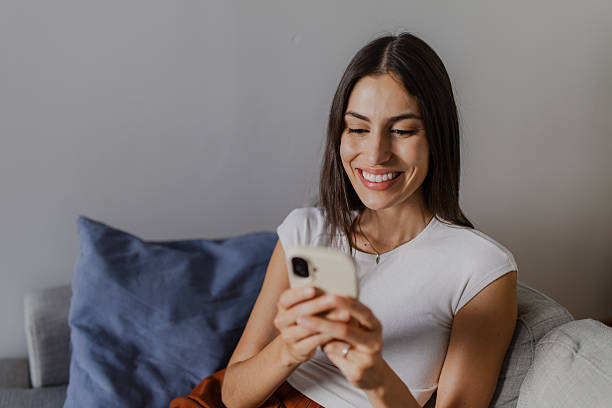 istock Smiling woman using smartphone while relaxing on sofa at home 2222611685