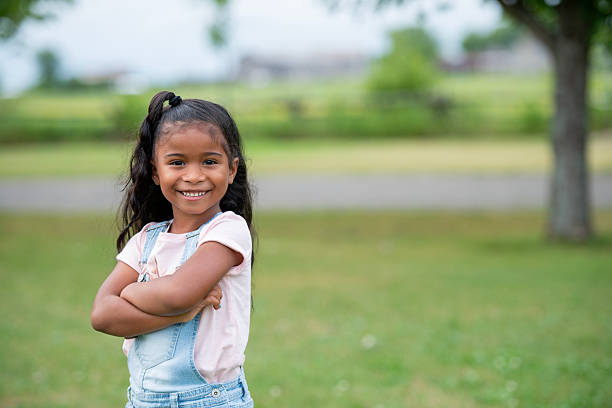 istock Smiling Young Girl Standing Outdoors on Grass With Folded Arms 2222612695