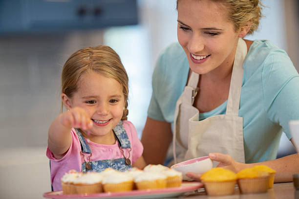istock Mother and Daughter Smiling While Decorating Cupcakes in a Modern Kitchen 2222622094