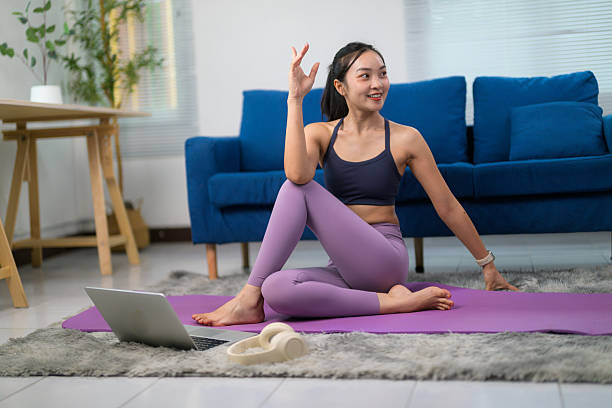 istock Young Asian woman practicing yoga at home, following an online tutorial on her laptop, embracing wellness and tranquility in her living room 2222624916