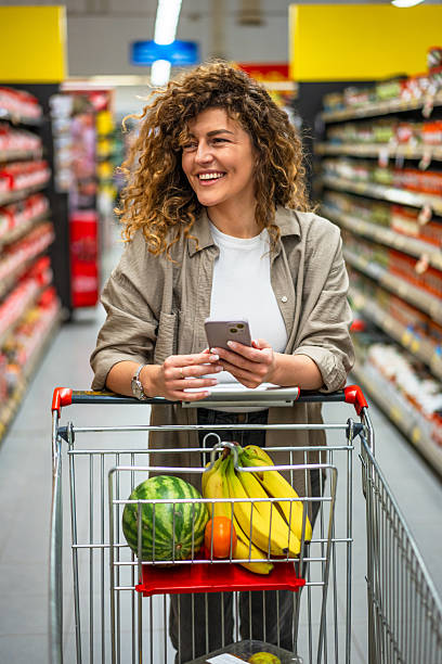 istock Smiling woman using smartphone while shopping in supermarket 2222631702