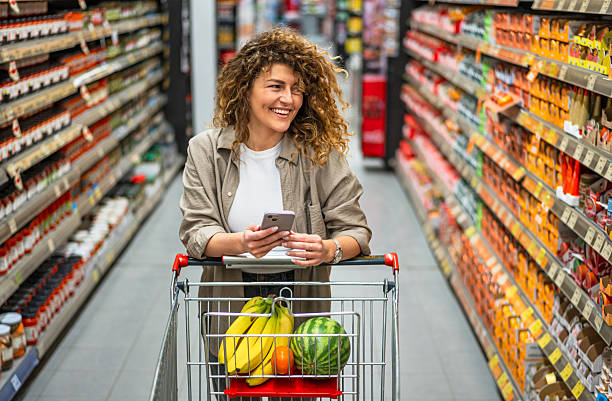 istock Smiling woman using smartphone while shopping in supermarket 2222632574
