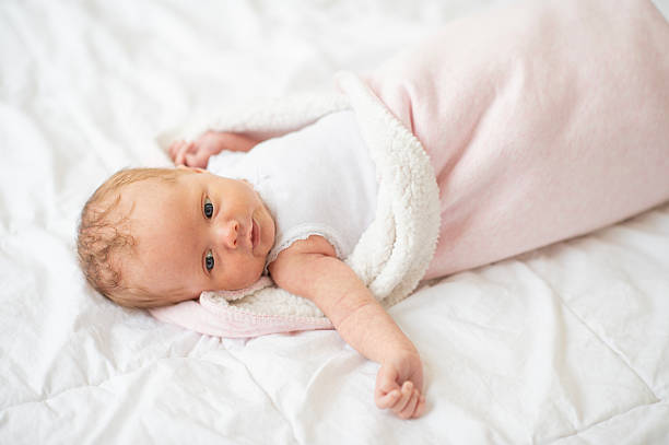 Cute newborn baby lies wrapped in a soft pink blanket on a white surface, presenting a serene and innocent moment reflecting warmth, safety, and peacefulness.