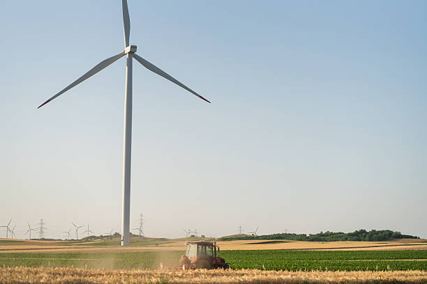 Agricultural tractor is working on the field with wind turbines