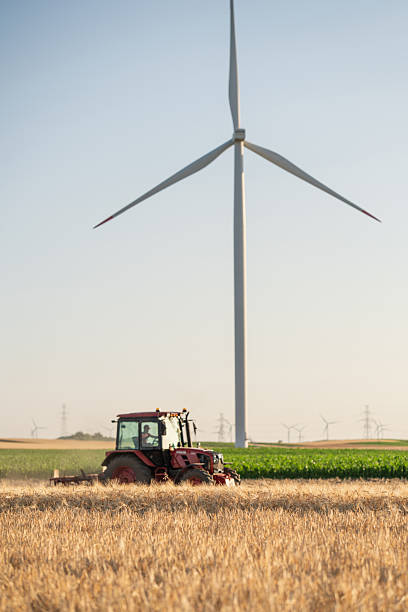istock Agricultural tractor is working on the field with wind turbines 2222636303