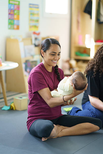 istock Young Woman Smiling While Holding a Baby in a Bright Classroom 2222638582