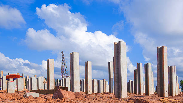 Many precast concrete piles foundation structure on the ground with pile driver machine in industrial factory building construction site against clouds on blue sky background