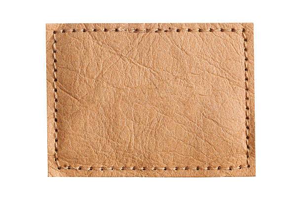 istock Brown leather patch closeup. Empty stitched label isolated on white background. Blank textured tag. Real leather surface with natural wrinkles. 2222646563