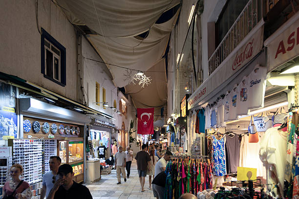 BODRUM, TURKEY - JUNE 29: Tourists walk through a lively bazaar street lined with clothing and souvenir shops under shade cloths in Bodrum on June 29, 2025, in Bodrum, Turkey. This shopping area is a popular destination for visitors exploring the coastal town.