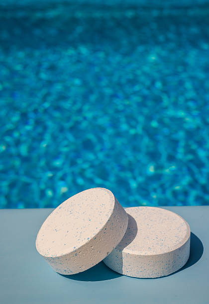 istock Two round chlorine tablets with blue specks lying on the poolside edge against a sparkling blue swimming pool background, used for water disinfection and care. 2222647805