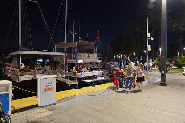 BODRUM, TURKEY - JUNE 29: People walk along the illuminated marina with moored yachts and sailing boats in Bodrum, Turkey, on June 29, 2025. The harbor area becomes a lively attraction point for evening strolls during the summer season.