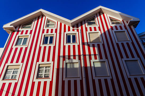 A low-angle view captures the striking facade of a building adorned with bold red and white vertical stripes and various windows, standing vibrantly against a deep blue sky