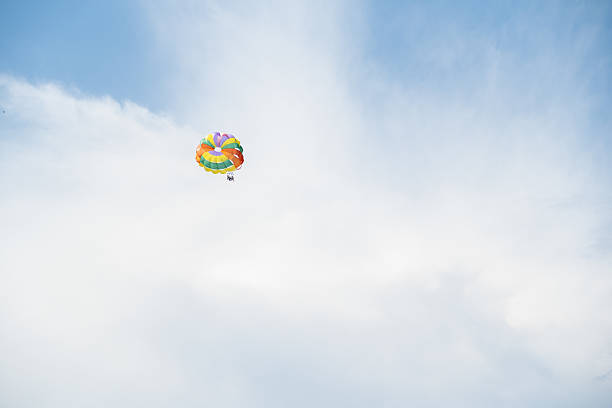 A colorful parachute glides gracefully in the sky, showcasing the thrill of parasailing and the beauty of the vast blue atmosphere beneath a few soft clouds.