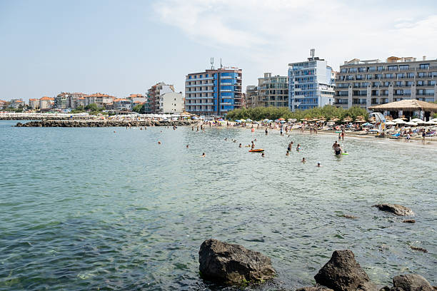 A lively beach scene showcasing people swimming, sunbathing, and enjoying various activities under a clear blue sky, highlighting leisure and relaxation by the sea.