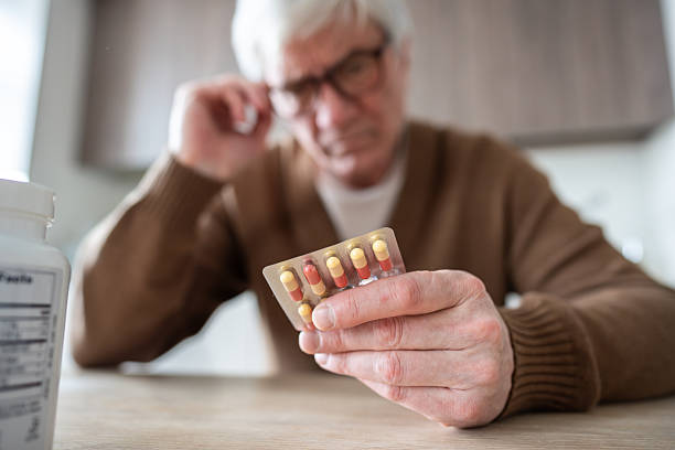 Pill blister check. Elderly man holds medication blister pack reading instructions with focused look
