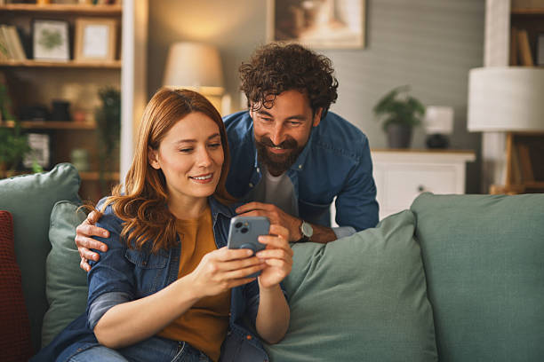istock Happy couple relaxing on sofa browsing smartphone at home 2222660016