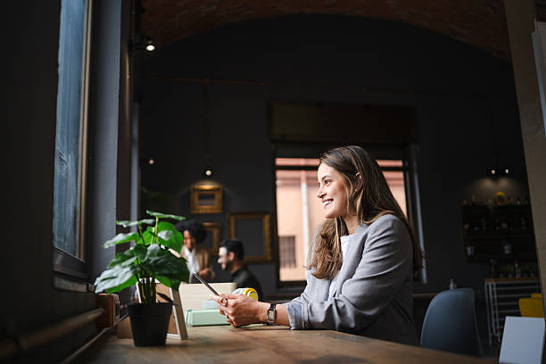 istock Professional woman working on digital tablet, smiling while drinking coffee at cafe table, experiencing workplace flexibility 2222660100
