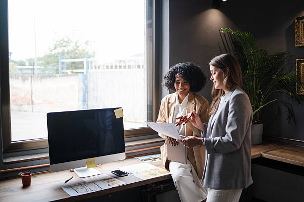 istock Two smiling businesswomen reviewing documents together in a modern office, showcasing teamwork and collaboration 2222660159