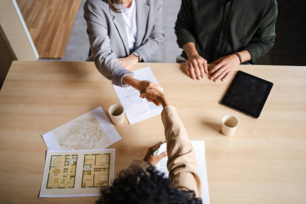 Architect shaking hands with client in the office, celebrating the successful closing of a deal while reviewing detailed blueprints