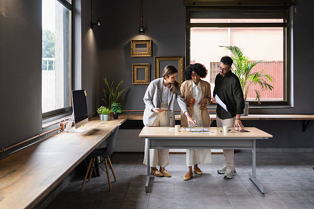 Three designers are collaborating on a new project, reviewing blueprints and discussing ideas in a modern office setting