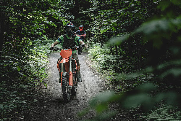 Saint-Mathieu-de-Parc, Québec, Canada, June 21, 2025. Two people riding motocross-style dirt bikes on a wooded trail at Camping du Parc in Saint‑Mathieu‑du‑Parc, Quebec, Canada. Depicts outdoor recreation and motor sport in a forested setting.