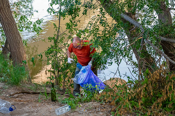 A volunteer collecting plastic and packaging trash on a riverbank in a forest landscape. Trash in a wooded area along the Duero River, Tordesillas, Valladolid, Castile and León, Spain - June 4, 2025.