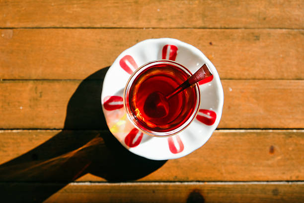 Turkish tea with deep red color served in a tulip-shaped glass on a wooden table, under sunlight.