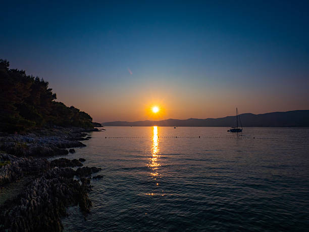 Sunset at Prva Voda beach in Split, Croatia, with a sailboat silhouetted on the Adriatic Sea, rocky shores, and golden skies—an idyllic Mediterranean escape.