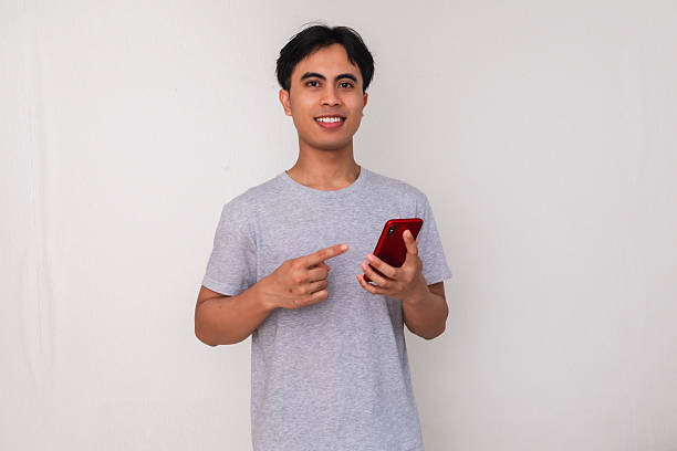 istock Portrait of a happy young Southeast Asian man smiling while using his smartphone on a white background, perfect for digital ads, promotions, or modern communication themes 2222688951