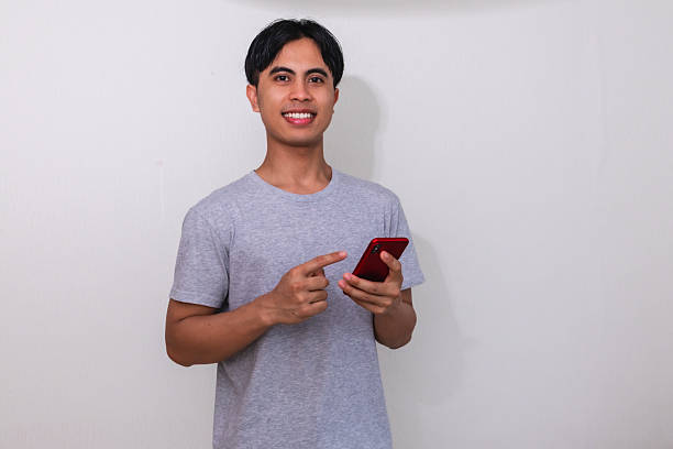 istock Portrait of a happy young Southeast Asian man smiling while using his smartphone on a white background, perfect for digital ads, promotions, or modern communication themes 2222689015