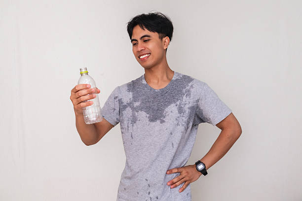 Young Asian man sweating and smiling while holding a water bottle and showing a satisfied gesture, isolated on white background, perfect for health and advertisement themes