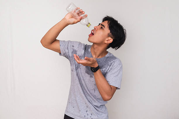istock Tired young Asian man sweating and holding an empty water bottle with a disappointed expression, isolated on white background. Concept of dehydration, heat, or thirst 2222689150